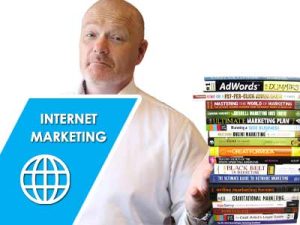 An image of John McLauchlan wearing a white shirt behing a stack of online business books